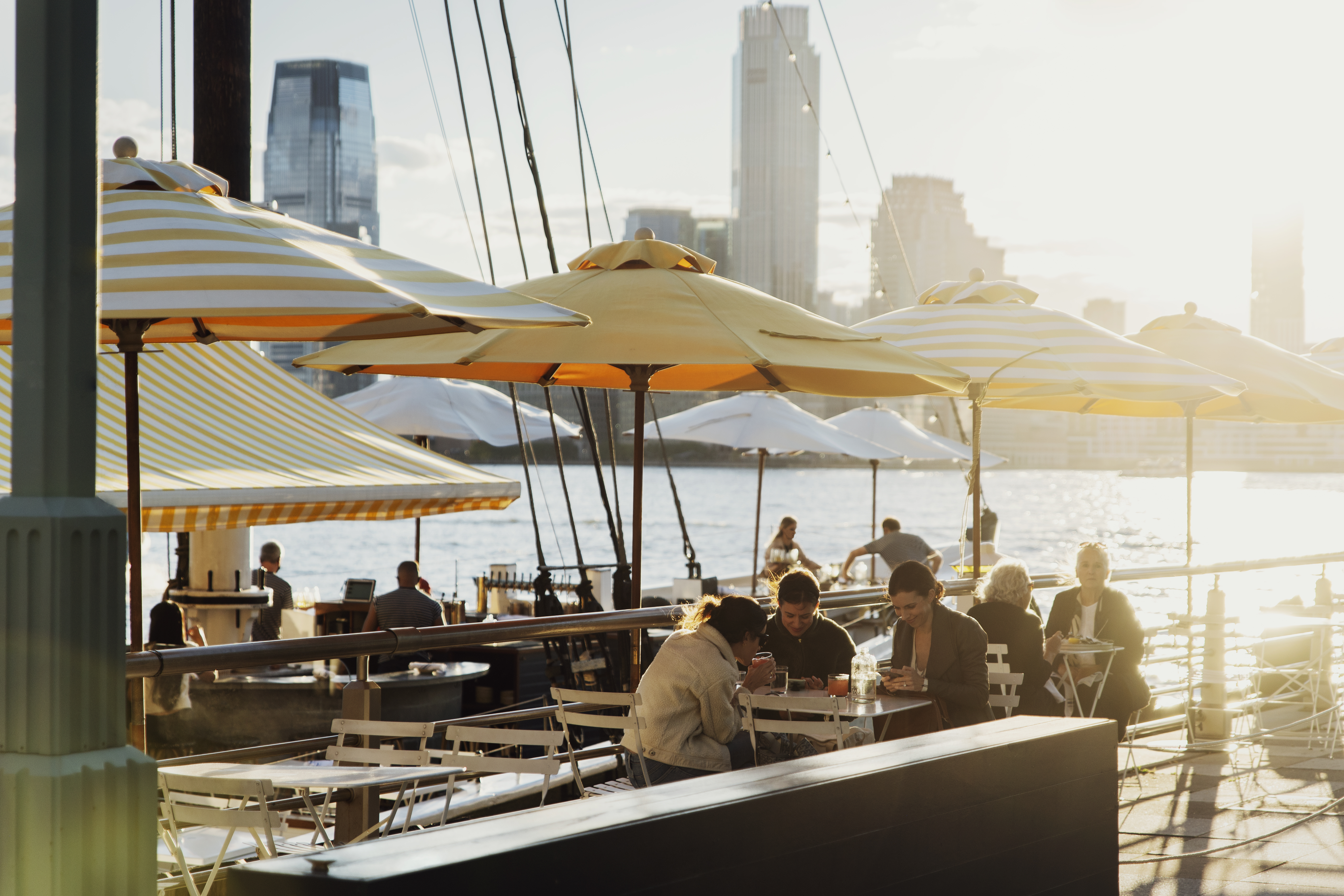 People eating at a restaurant on a river with yellow table umbrellas 