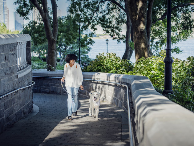 Woman walking with a golden retriever on a stone path in an urban park surrounded by trees
